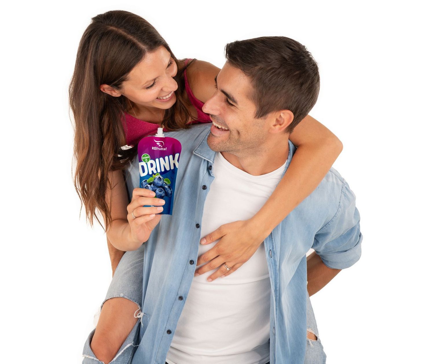 Ein junger Mann trägt eine Frau huckepack, während sie gemeinsam in die Kamera lächeln und eine Packung Heidelbeer-Trinkjoghurt halten.