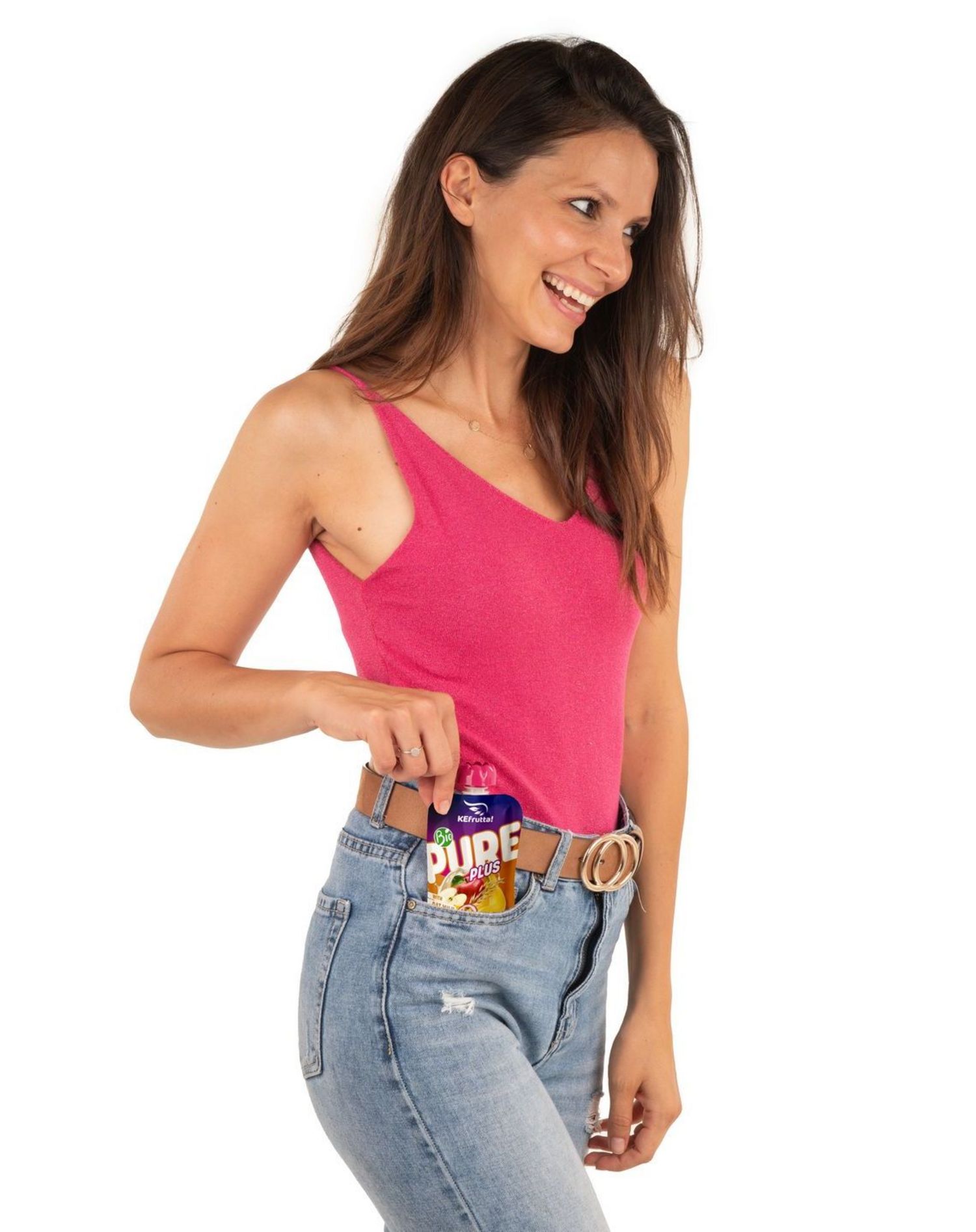 Eine lächelnde Frau mit langem braunen Haar trägt ein pinkes Tanktop und Jeans und steckt ein Obstpüree-Quetschbeutel in ihre Hosentasche.