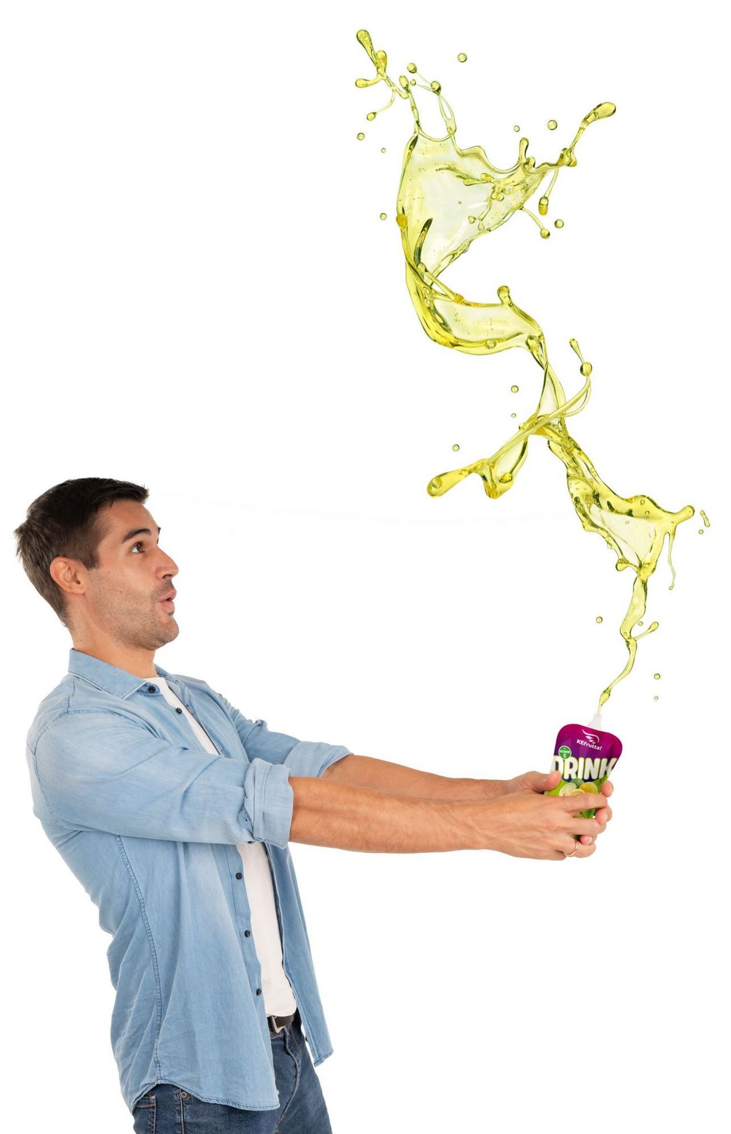 Ein junger Mann in einem blauen Jeanshemd hält einen kleinen Getränkebeutel, aus dem ein großer, dynamischer Spritzer gelber Flüssigkeit nach oben explodiert.